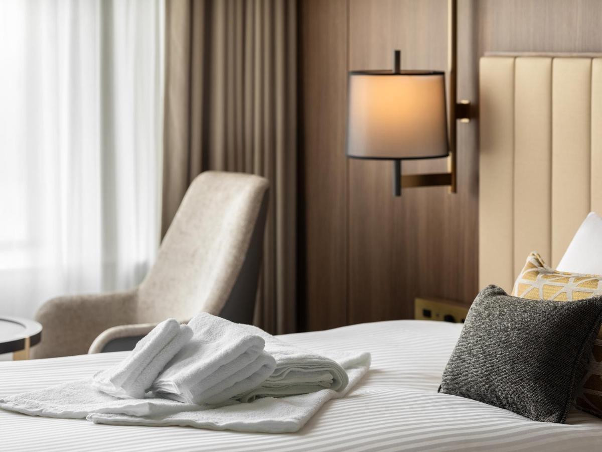 Mitsui Garden Hotel Roppongi Tokyo Premier Dış mekan fotoğraf The image shows a stylish hotel room. In the foreground, there is a neatly made bed with white linens, featuring a stack of white towels arranged in a decorative manner. To the side, there is a gray upholstered armchair and a small table. The backgro
