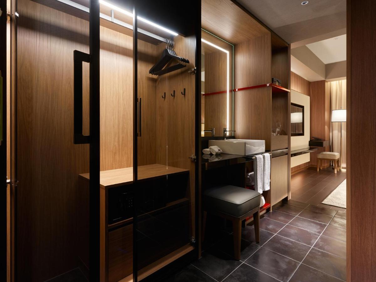 Mitsui Garden Hotel Roppongi Tokyo Premier Dış mekan fotoğraf The photo depicts a modern and stylish hotel room's closet area. It features wooden cabinetry with a sleek finish, including mirrored doors. Inside, there are hangers for clothing and hooks mounted on the wall. A small bench or chair is positioned ne