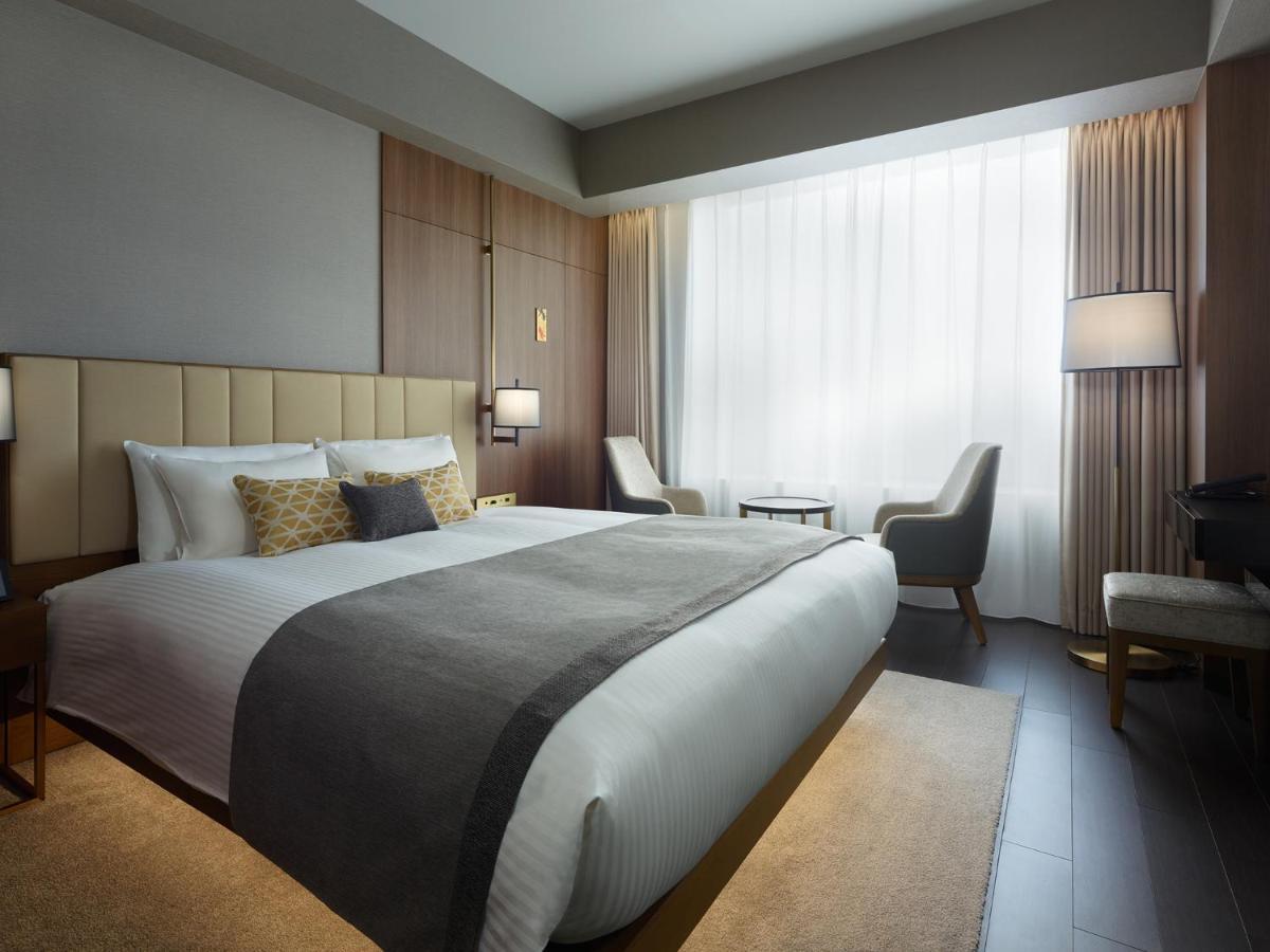 Mitsui Garden Hotel Roppongi Tokyo Premier Dış mekan fotoğraf The photo shows a modern hotel room featuring a large bed with a neatly arranged white and gray bedding. The headboard is upholstered in a light color, adding to the room's contemporary design. On either side of the bed, there are bedside lamps provi