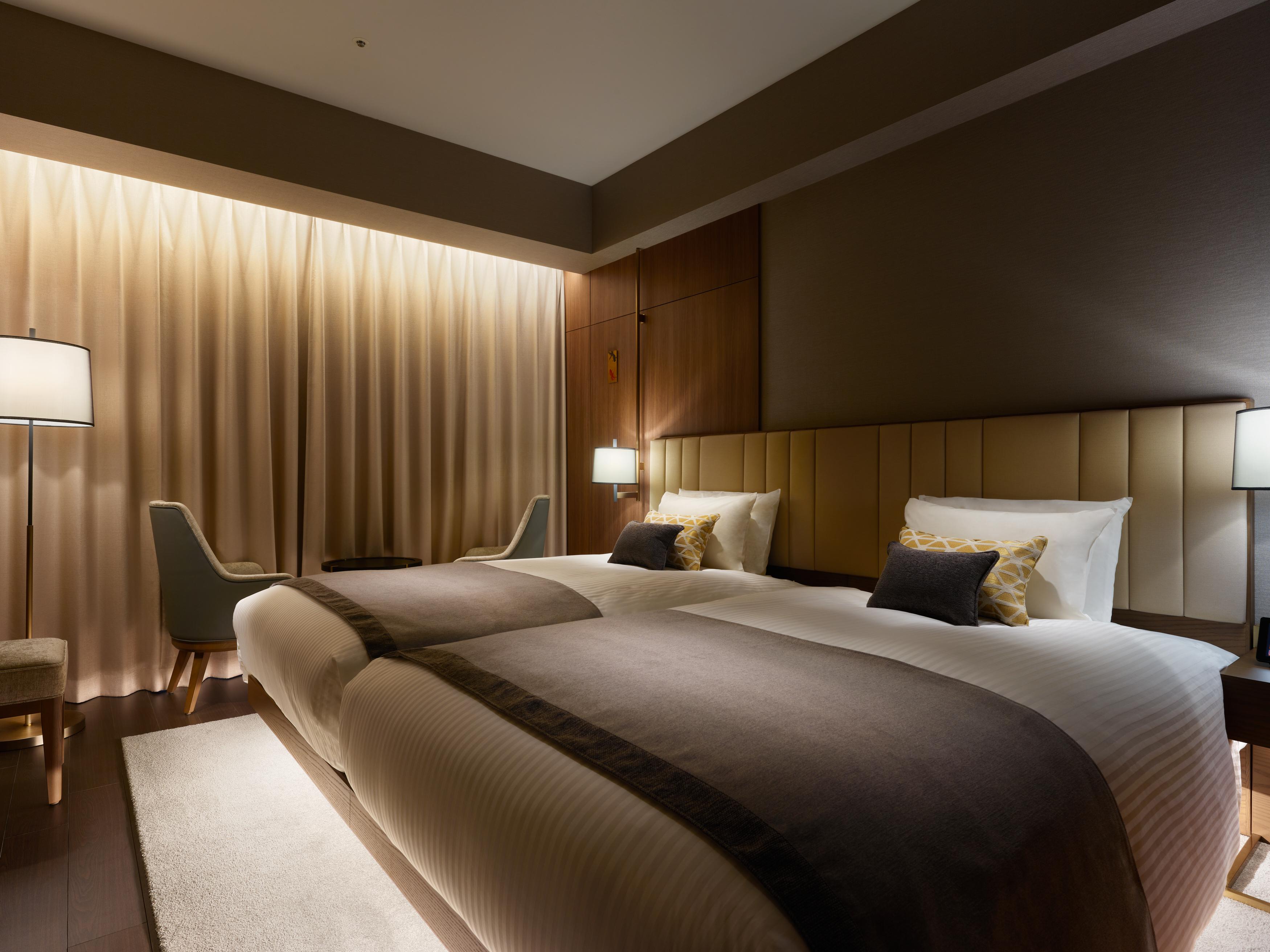 Mitsui Garden Hotel Roppongi Tokyo Premier Dış mekan fotoğraf The photo shows a modern hotel room featuring two twin beds with elegant bedding. The room is adorned with soft, neutral tones and has a warm ambiance created by subtle lighting. A pair of bedside lamps provide additional light, and there is a cozy c