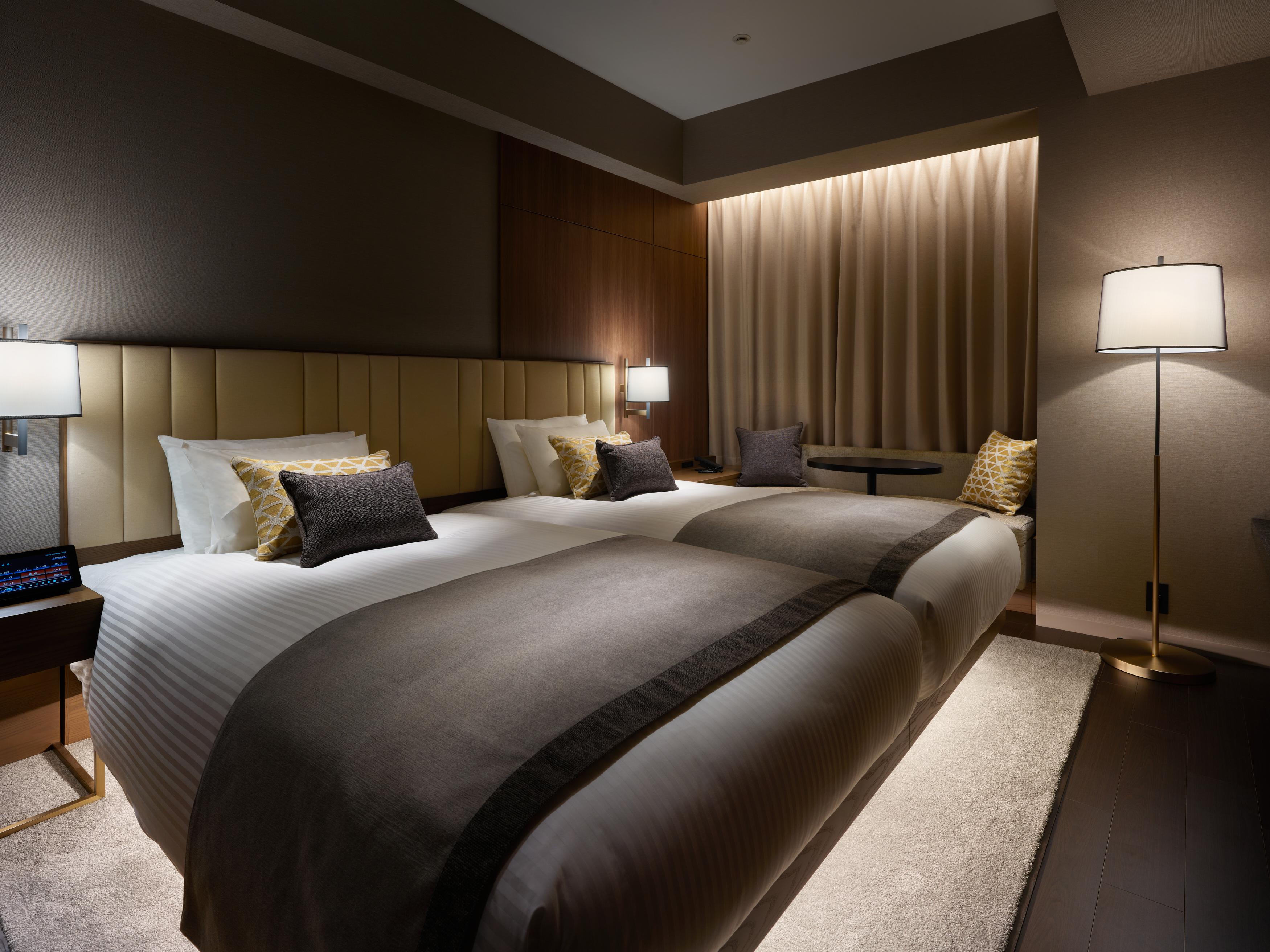 Mitsui Garden Hotel Roppongi Tokyo Premier Dış mekan fotoğraf The photo shows a modern hotel room featuring two beds with elegant bedding in neutral colors. Each bed is adorned with decorative pillows. The room has a sophisticated ambiance with dim lighting, highlighted by table lamps on either side of the beds