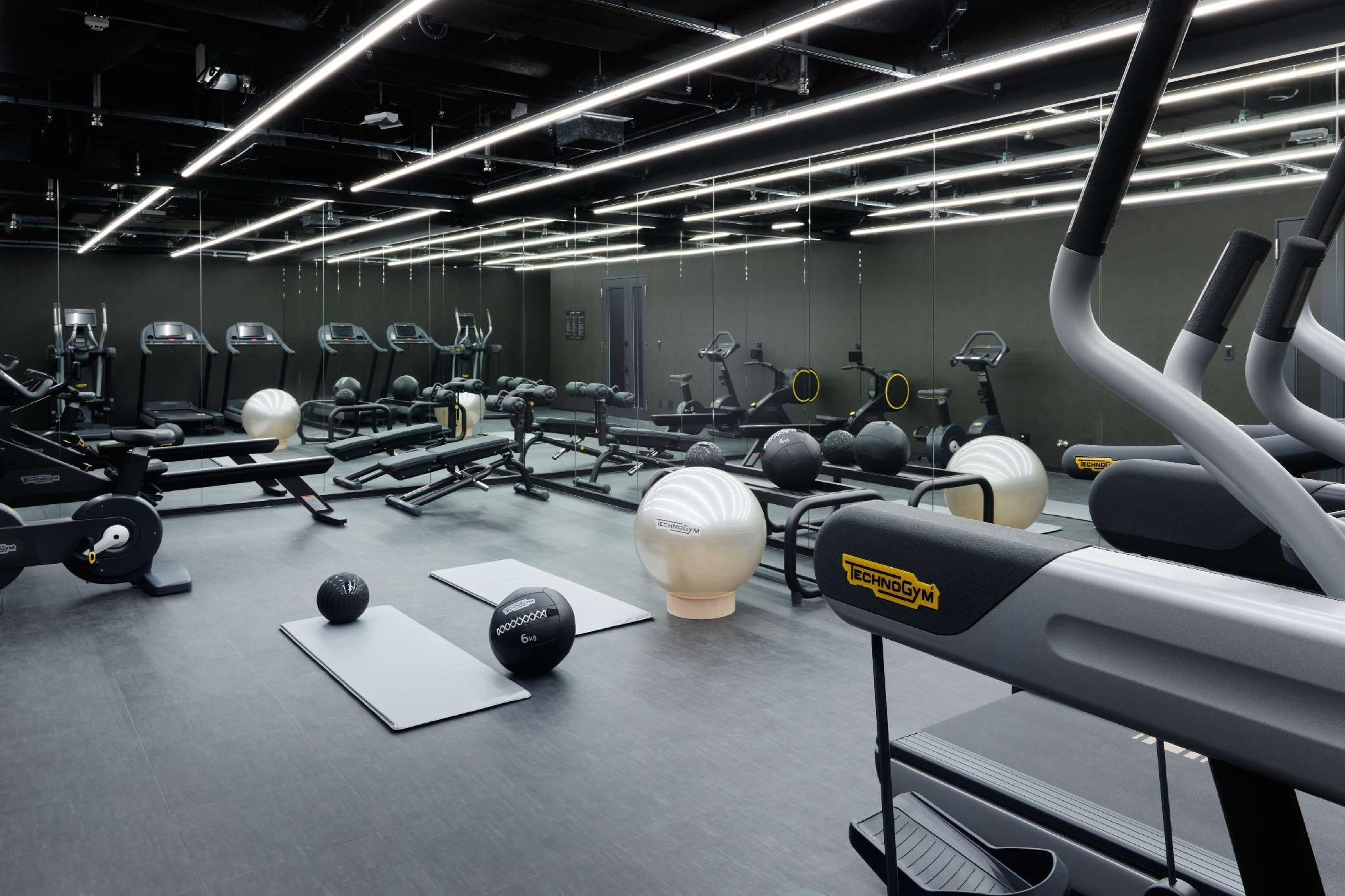 Mitsui Garden Hotel Roppongi Tokyo Premier Dış mekan fotoğraf The photo shows a modern gym interior. The space features various exercise equipment, including cardio machines like treadmills and elliptical trainers, weight machines, and free weights. There are also exercise mats and fitness balls scattered throu
