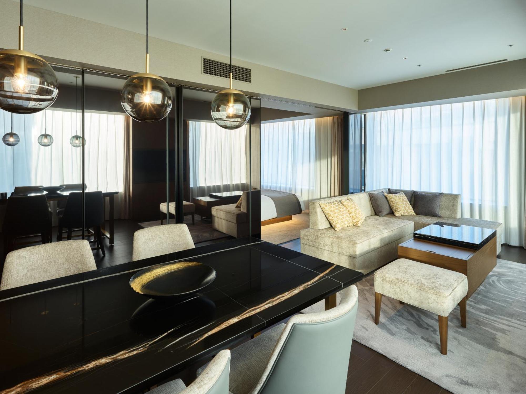 Mitsui Garden Hotel Roppongi Tokyo Premier Dış mekan fotoğraf The photo shows a modern and stylish living area. It features a dining table with elegant chairs, a comfortable seating area with a light-colored sofa, and a coffee table. The room is well-lit by large windows draped with sheer curtains, allowing nat