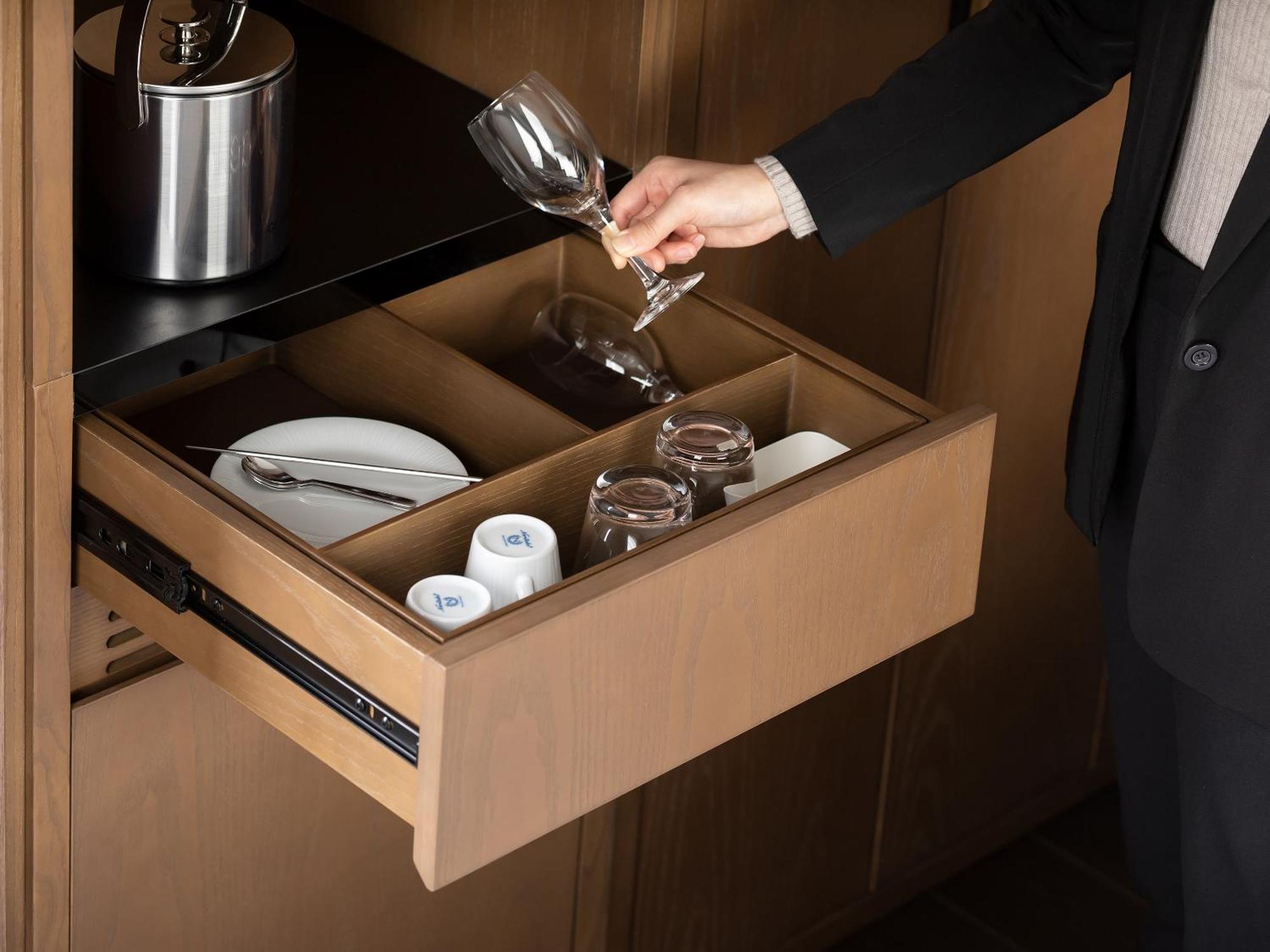 Mitsui Garden Hotel Roppongi Tokyo Premier Dış mekan fotoğraf The photo depicts a wooden kitchen drawer being pulled open, revealing a neatly organized selection of dishware. Inside, there are glass cups, a wine glass being held by a person, and plates. The setting appears modern and sleek, with a sophisticated